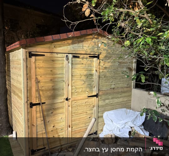 מחסן עץ עם דלתות כפולות וכלי עבודה בגינה